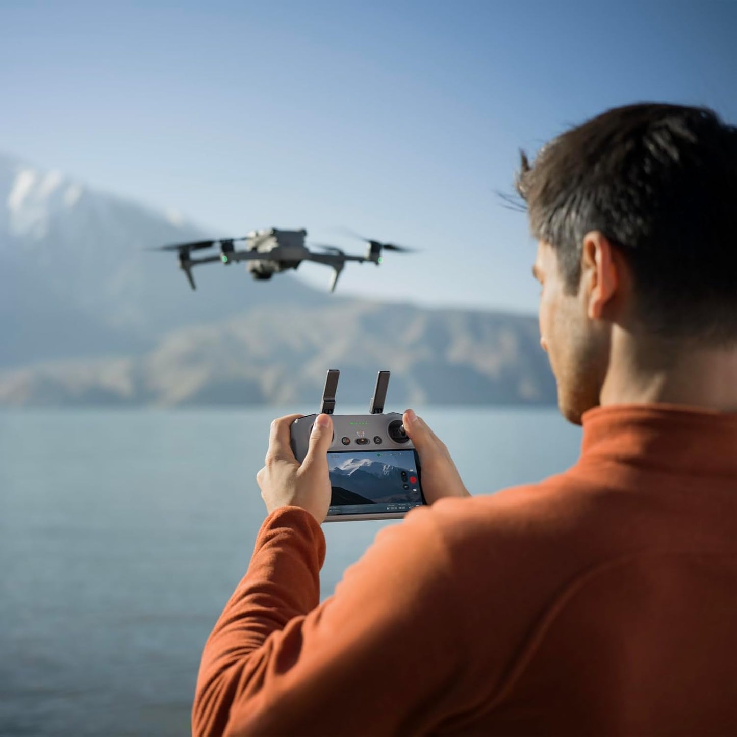 A person operating a DJI Air 3S 4K drone with a control device over a scenic landscape.