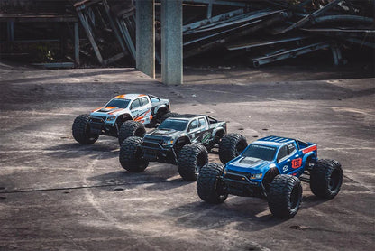 Three remote-controlled FMS 1/24 Chevrolet Colorado monster trucks on a concrete surface with industrial background