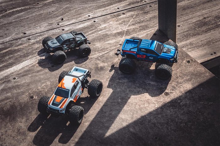 Three FMS 1/24 Chevrolet Colorado off-road monster trucks on a textured surface