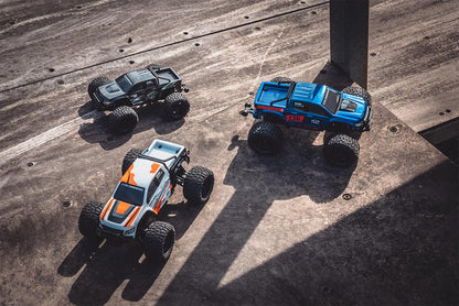 Three FMS 1/24 Chevrolet Colorado off-road monster trucks on a textured surface