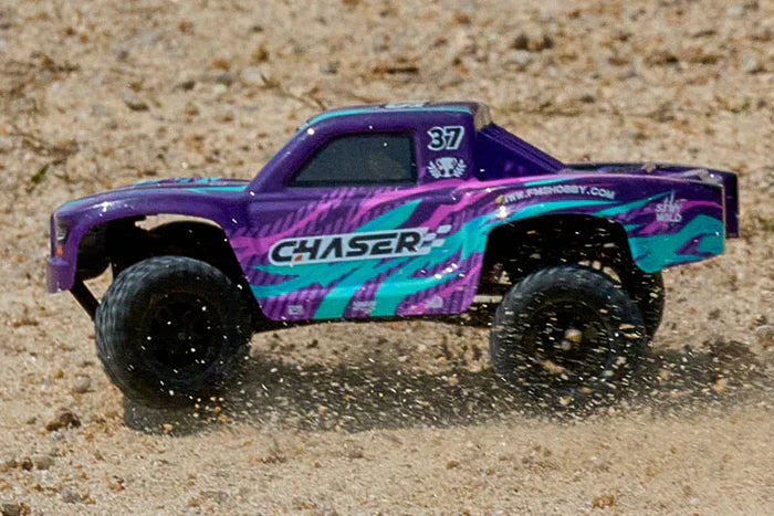 FMS FSC24 Chaser in sand action - front three-quarter view of purple and green truck accelerating on loose sand, dust flying, LED lights active, high-speed drift