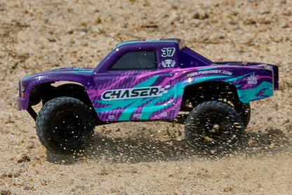 FMS FSC24 Chaser in sand action - front three-quarter view of purple and green truck accelerating on loose sand, dust flying, LED lights active, high-speed drift