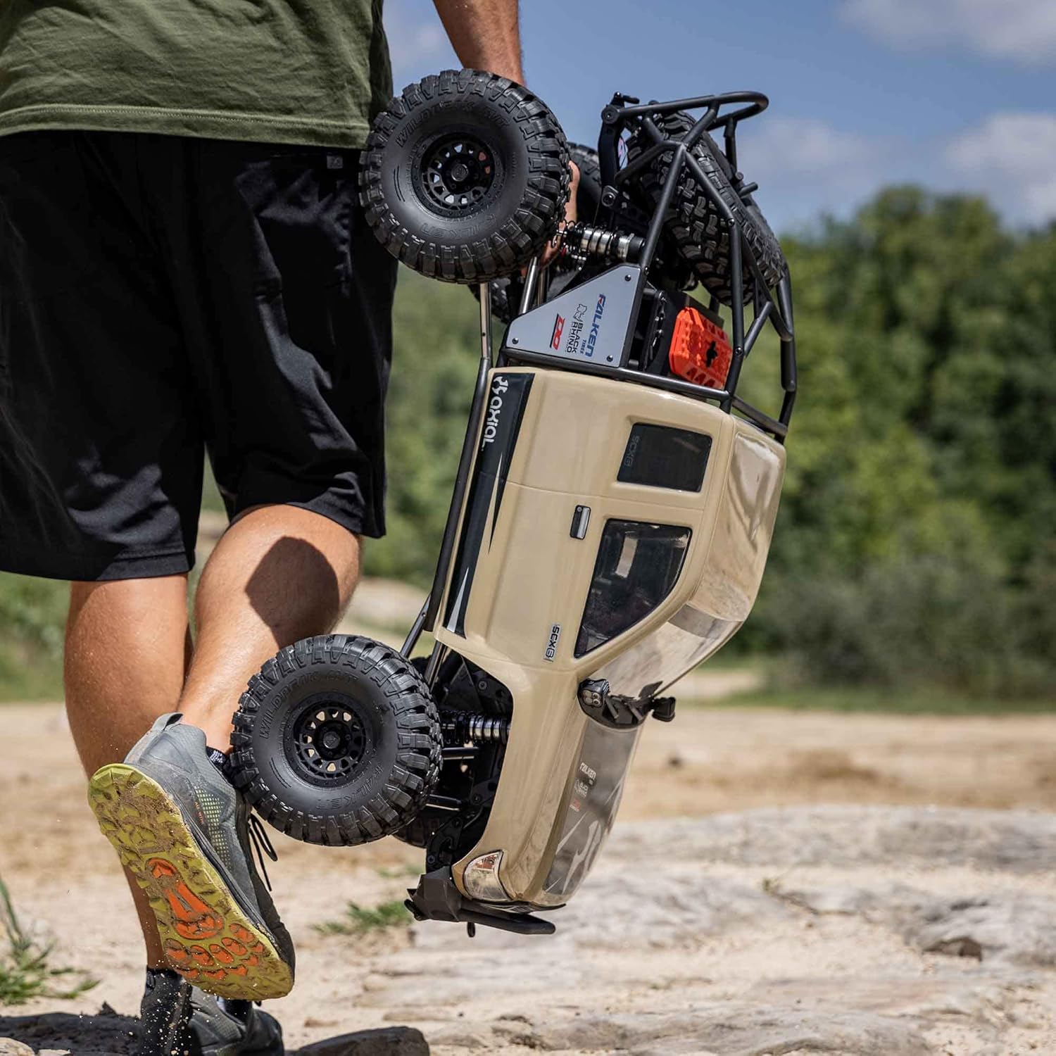 Axial SCX6 Trail Honcho 1/6 scale 4WD RTR rock crawler – person carrying a remote-controlled off-road vehicle in an outdoor setting, blue body, massive tires