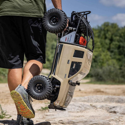 Axial SCX6 Trail Honcho 1/6 scale 4WD RTR rock crawler – person carrying a remote-controlled off-road vehicle in an outdoor setting, blue body, massive tires