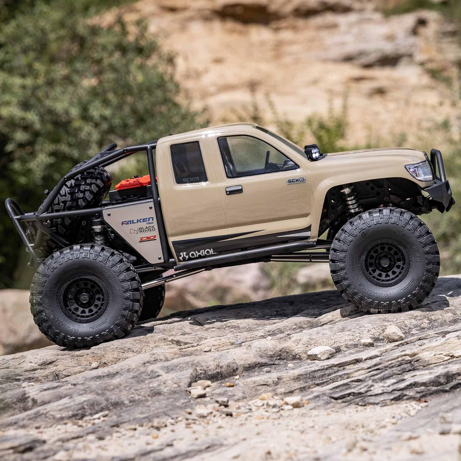 1/6 scale Axial SCX6 Trail Honcho RC crawler – beige off-road vehicle climbing rocky terrain with trees background, detailed suspension, realistic scale