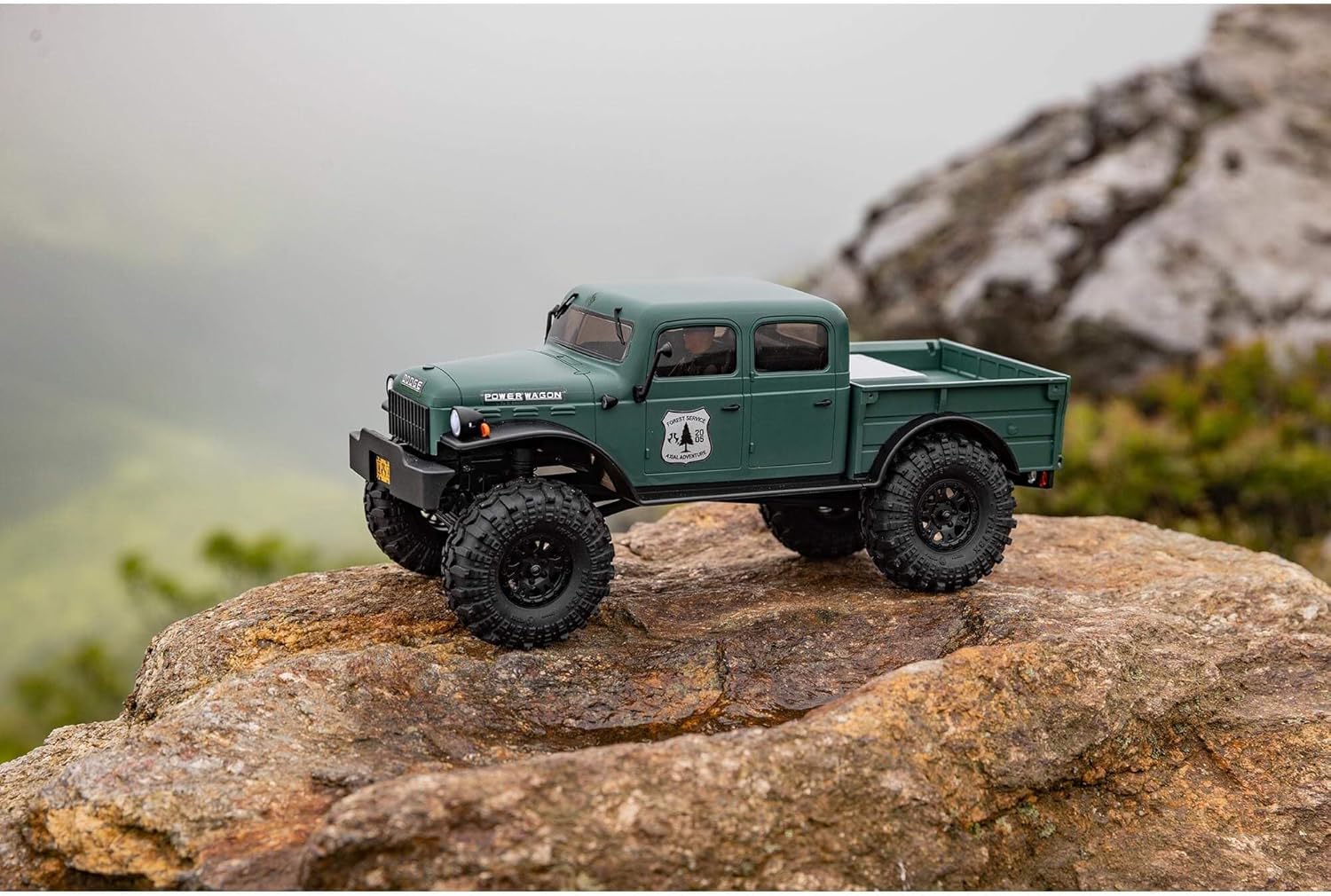 Axial 1/24 SCX24 Power Wagon crawler green truck on a rocky surface with a mountainous background